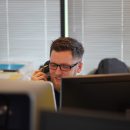 man using landline phone sat behind two computer screens