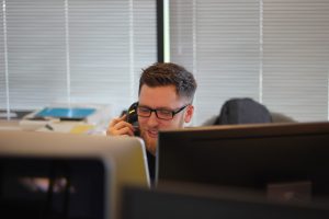 man using landline phone sat behind two computer screens